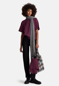 Bordowa, oversize koszulka, szary szalik, czarne spodnie i masywne czarne botki. Uzupełniona wzorzystą torbą na ramię i złożonym fioletowym materiałem.