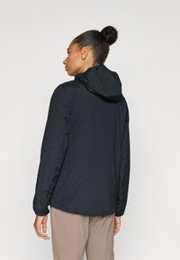 Casaco leve preto com capuz, apresentando uma textura suave e punhos elásticos. A parte de trás tem uma bainha ligeiramente curva. Design em cor sólida.