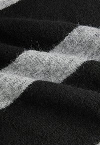 Tissu en laine noir et gris avec un motif en zigzag texturé ; surface douce et pelucheuse ; plis courbés créent de la profondeur et de la dimension.