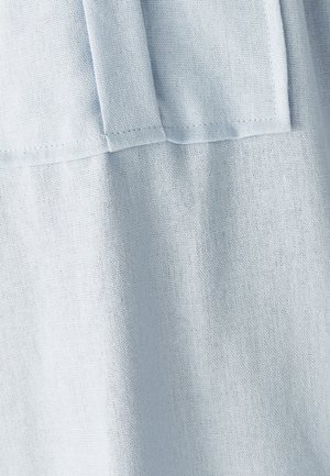 Helehelesinine sinine kangas, millel on nähtavad õmblused ja volditud õmbluse detail, näidates tekstuuri ja peent varjundit.