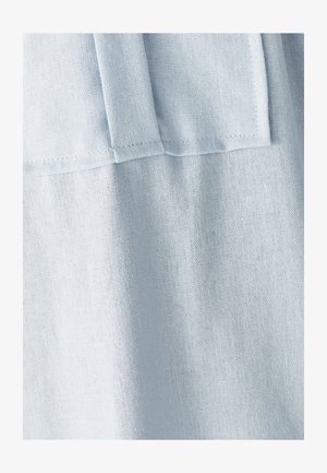 Helehelesinine sinine kangas, millel on nähtavad õmblused ja volditud õmbluse detail, näidates tekstuuri ja peent varjundit.