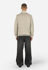 Beżowy, prążkowany top z długim rękawem i wysokim kołnierzem, w zestawieniu z ciemnoszarymi, luźnymi dżinsami z dużymi tylkami i kontrastowymi szwami.