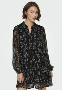 Abito nero trasparente con un motivo floreale in rosa e verde, abbottonatura frontale, scollo a balze e maniche lunghe e puffate.