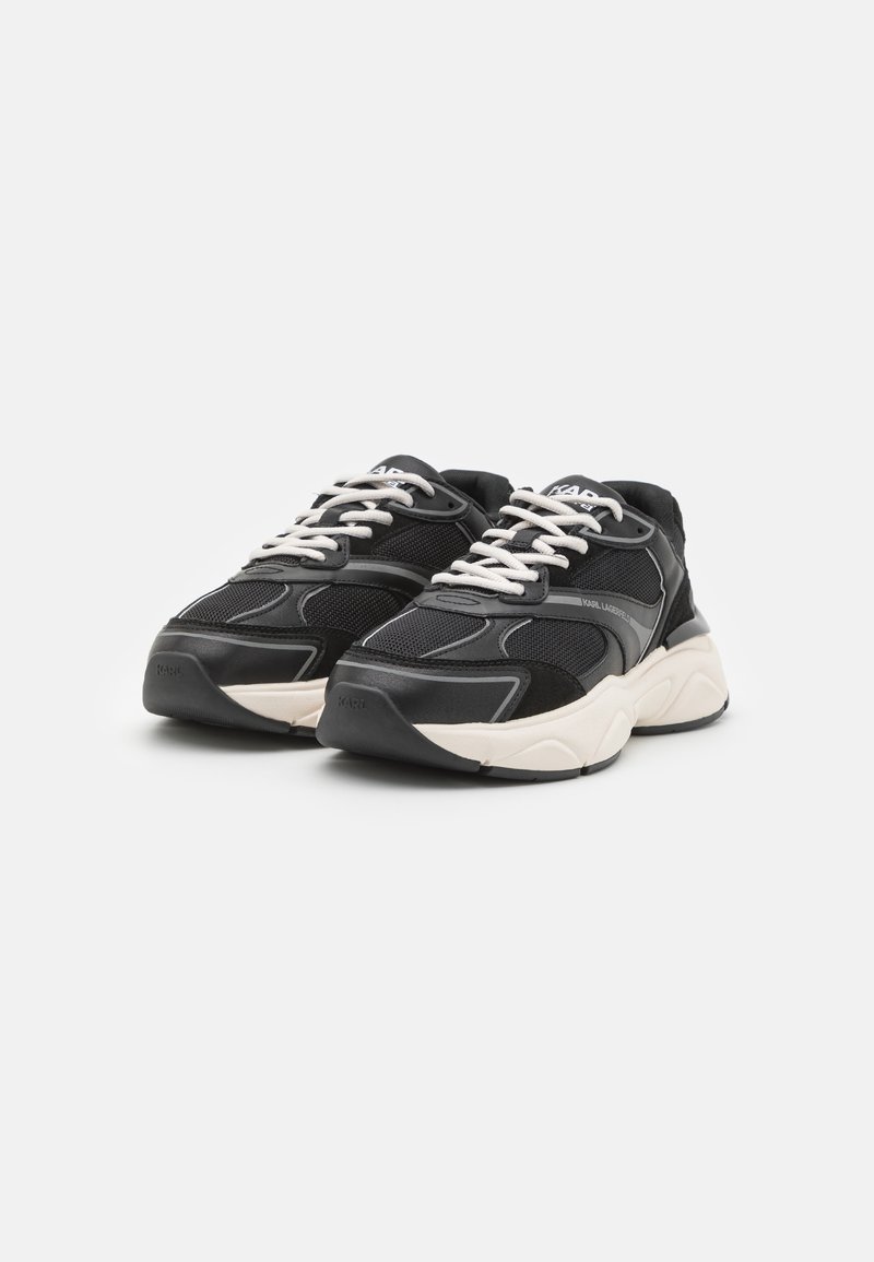 Baskets noires avec des matériaux en maille et en cuir ; forme arrondie, semelle épaisse couleur crème et lacets et accents contrastants.