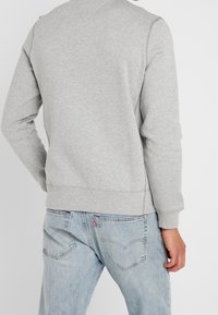 Sudadera de algodón gris con puños y dobladillo de canalé, con un diseño sin costuras, combinada con unos vaqueros de mezclilla azul claro.