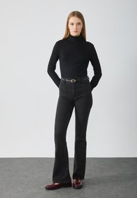 Haut noir à col roulé associé à un pantalon en denim noir taille haute évasé, avec poches et une boucle de ceinture en métal. Chaussures bordeaux brillantes.