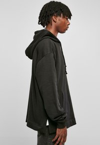 Svart, oversized hettegenser med snøring på hetta, lange ermer og frontlomme. Stoffet ser mykt ut med en jevn tekstur og avslappet passform.