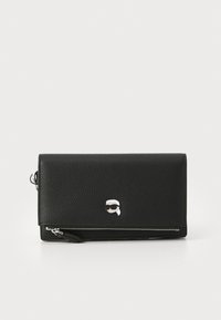 Portefeuille en cuir noir avec une surface texturée et des accessoires en argent. Dispose d'un compartiment zippé et d'un emblème décoratif distinctif.