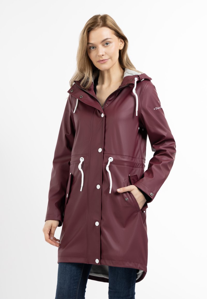 Lange bordeauxrode regenjas van waterdicht materiaal, voorzien van een capuchon, witte accenten, trekkoorden, drukknoopsluiting en twee voorzakken.