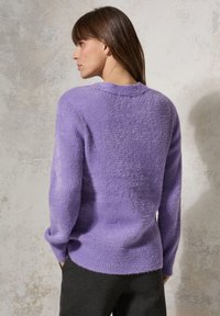 Lila stickad tröja med texturerad yta, rund halsringning och ribbade fickor samt nederkant. Lätt material, avslappnad passform och långa ärmar.