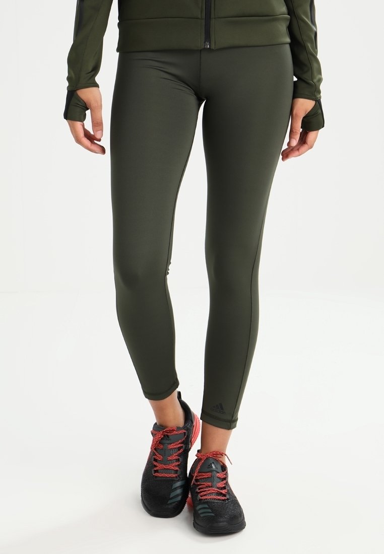 Oliwkowe legginsy sportowe z elastycznego materiału, charakteryzujące się smukłym designem. W połączeniu z czarnymi butami z czerwonymi akcentami i sznurówkami.