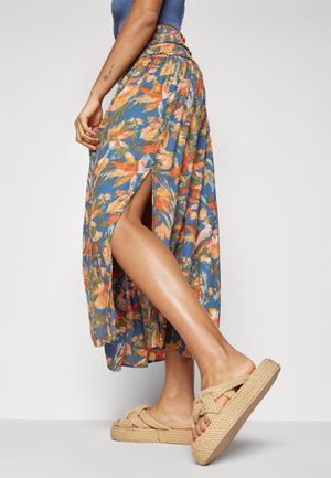 Luchtige maxi-rok met bloemmotief en een zijsplit, met een blauwe basis en oranje, groene en gele bloemenpatronen. Gecombineerd met gevlochten slippers.