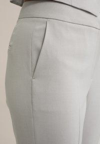 Light grey tailored trousers with a smooth texture, featuring a flat front, side pockets, and subtle pleats along the waistband.