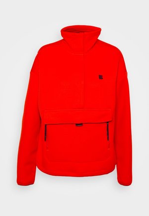 Kirkkaanpunainen fleece-pullover takki korkealla kauluksella, pitkät hihat, suuri etutasku vetoketjulla ja pieni musta logo rinnassa.
