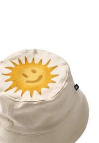 Beiger Fischerhut mit einer strukturierten gelben Sonnen-Grafik auf der Oberseite, die ein Lächeln und Strahlendetails zeigt. Schwarzes Etikett an der Seite.