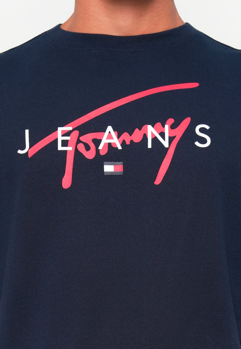 T-shirt en coton bleu marine avec un texte cursif rouge audacieux "Tommy" et des lettres blanches "JEANS", accompagnés d'un petit détail stripe de logo.