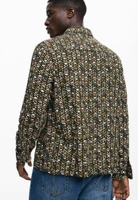 Mustriline jakk tumerohelises, pruunis ja valges, millel on krae ja elastsed mansetid. Kude on tekstuuriga, kudumise välimusega.