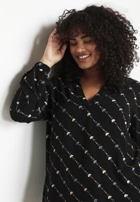 Black shirt featuring a floral pattern in blue, brown, and cream. Long sleeves with gathered cuffs and a relaxed collar. Lightweight fabric.