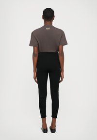 Brown short-sleeve shirt with small logo at the back, paired with fitted black leggings. Smooth fabric texture, form-fitting design.