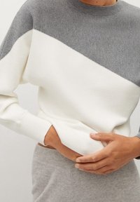 Knit pullover with a round neckline, featuring a color-block design in gray and cream. Ribbed cuffs and hem, soft texture.