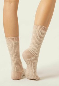 Calzini a coste rosa chiaro con una texture morbida, caratterizzati da un design a maglia adattabile e strisce crema a contrasto. Altezza alla caviglia con tallone rinforzato.