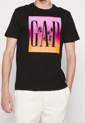 Zwarte katoenen T-shirt met een roze en oranje gradient vierkant met daarin de tekst "GAP" en palmboomgraphics in het zwart. Korte mouwen.