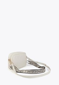 White quilted crossbody bag with a logo strap, positioned at an angle against a plain background. Zippered top and gold accents visible.