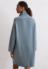 Jasnoniebieska, oversize sukienka swetrowa z wysokim kołnierzem, wykonana z miękkiego materiału. Posiada długie rękawy oraz zaokrąglony dół sięgający do połowy ud.