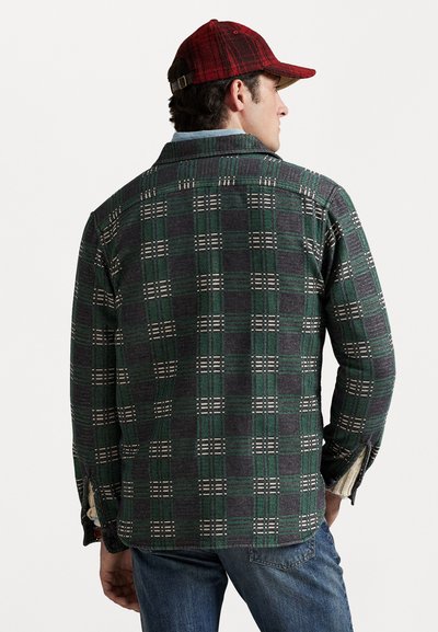 Zeleno-sivá károvaná košeľa na gombíky s bielymi detailami, s golierom, postrannými rozparkami a dlhými rukávmi. Nosí sa s modrými džínami a červenou čiapkou.