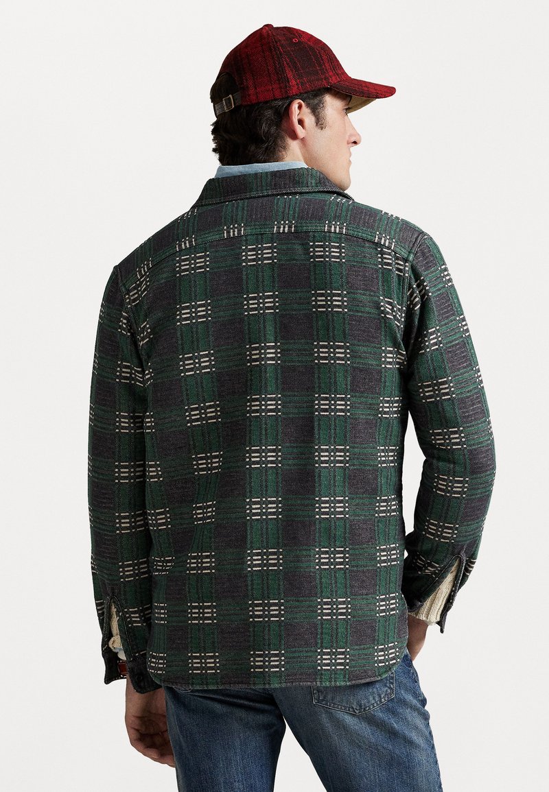 Grøn- og gråternet skjorte med knaplukning og hvide detaljer, med krave, sideslids og lange ærmer. Bæres med blå jeans og en rød kasket.