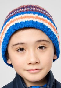 Bonnet en tricot avec des rayures bleues, oranges, blanches et rouges, présentant une texture côtelée. Porté sur une veste sombre, mettant l'accent sur le design du bonnet.