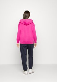 Sudadera con capucha rosa y puños acanalados, combinada con pantalones navy y zapatillas blancas. Textura suave, diseño casual y ajuste relajado.