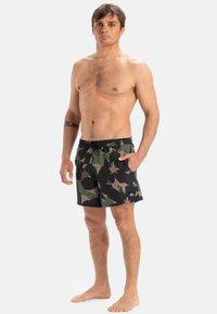 Mustat ja vihreät camouflage-uimashortsit, joissa on nyörillä säädettävä vyötärö, synteettistä materiaalia, lyhyt malli ja pieni logo vasemmassa alakulmassa.