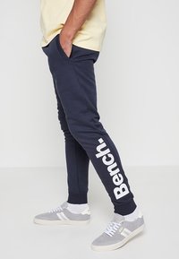 Marineblauwe joggingbroek met witte "Bench." branding langs het linkerbeen, gemaakt van een zachte, gestructureerde stof, met zijzakken en een tapered fit.