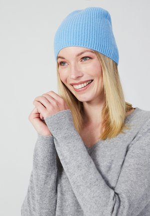Lichtblauwe geribbelde gebreide beanie, zachte textuur, aansluitend ontwerp. Gekozen in combinatie met een grijze trui met lange mouwen en een v-hals.