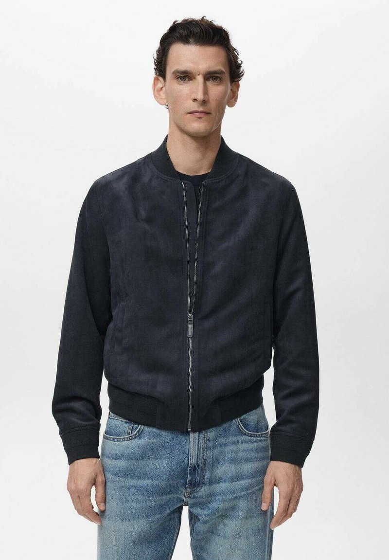 Chaqueta bomber de ante azul marino con puños y bajo de canalé, cierre frontal de cremallera y hombros sin costuras, combinada con jeans de color azul claro.