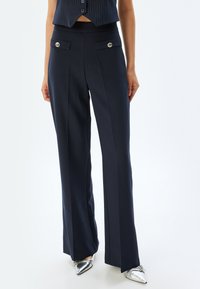 Marina vida byxor i bredde med slät tyg, hög midja och två framfickor med silverknappdetaljer.