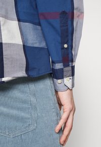 Multicolor geruit overhemd gemaakt van stof met een zachte textuur. Heeft een blauwgrijs palet, knoop manchetten en een afgeronde zoom. Corduroy broek zichtbaar.