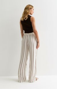 Haut sans manches marron côtelé associé à un pantalon large blanc avec des rayures verticales foncées ; le pantalon a un tissu texturé et une taille élastique.