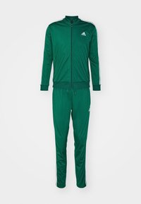 Zielony dres Adidas z białymi paskami na rękawach i nogawkach, kurtka zapinana na zamek błyskawiczny oraz elastyczne mankiety na rękawach i nogawkach.