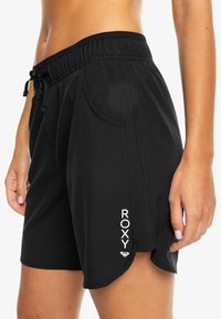 Shorts de sport noirs avec taille élastique, cordon de serrage, poches latérales et logo "ROXY" blanc près de l'ourlet. Tissu lisse et léger.