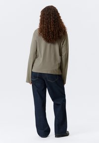 Olijfgroen langemouwen-shirt van zachte stof, gecombineerd met losvallende donkerblauwe jeans met lichte stiksels en een ontspannen silhouet.