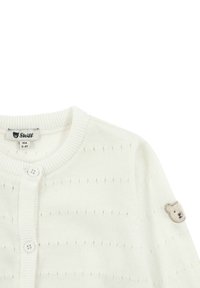 Bílý pletený cardigan s kulatým výstřihem, zapínáním na knoflíky a texturovaným vzorem. Výrazný detail: malé vyšívané medvídko na rukávu.