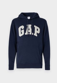 Sudadera con capucha de color azul marino, con un bolsillo canguro, cordón y el logotipo de "GAP" en gris claro en letras grandes en el pecho.