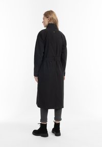 Zwarte trenchcoat met een hoge kraag, een ceintuur in de taille en lange mouwen. Gemaakt van een gladde stof, met een recht verloop en minimale accenten.