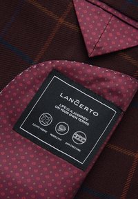 Bordowa tkanina w kratkę, z teksturowaną powierzchnią. Metka zawiera instrukcje dotyczące pielęgnacji oraz oznaczenia marek, a na kieszeni znajdują się małe motywy kwiatowe.