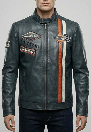 Homme portant une veste de course en cuir noir avec des bandes rouges et blanches, des écussons et des poches zippées, debout devant un fond uni.