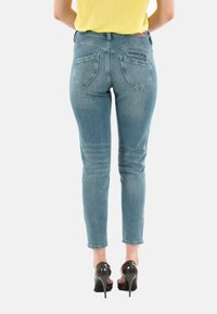 Jeans ajustados de color azul claro con una textura suave, que cuentan con dos bolsillos traseros, un bolsillo con cremallera y un dobladillo recortado. Llevados con tacones altos negros.