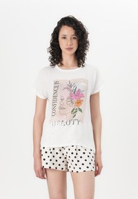 White graphic t-shirt featuring a floral design and metallic text "CONFIDENCE IS BEAUTY." Paired with polka dot shorts. Soft fabric, relaxed fit.