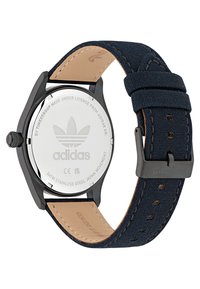 Juodas nerūdijančio plieno laikrodis su tamsiai mėlynu drobiniu dirželiu, pasižymintis lygia tekstūra ir rusvos odos apatine puse. "Adidas" logotipas išgraviruotas ant nugarėlės.